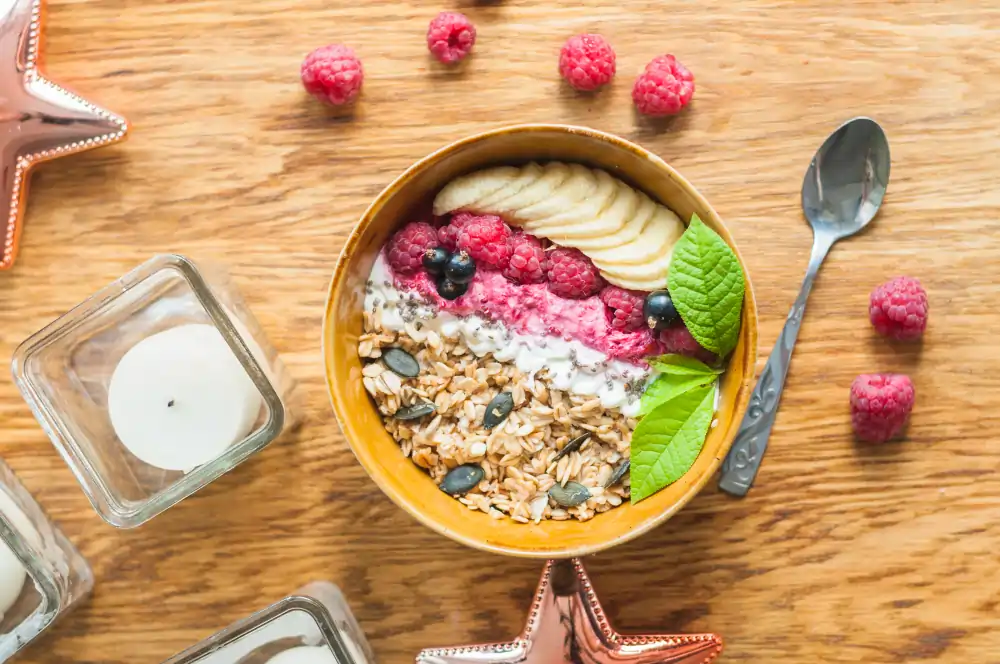 bowl healthy oatmeal with banana fresh berries and nuts in blow on wooden table with spoon